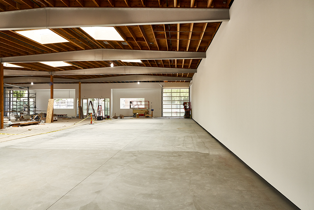 925 N. Orange interior — the open gallery floor under an exposed wood bow-truss ceiling with skylights, polished concrete underfoot and daylight through the glass bay doors at the far end
