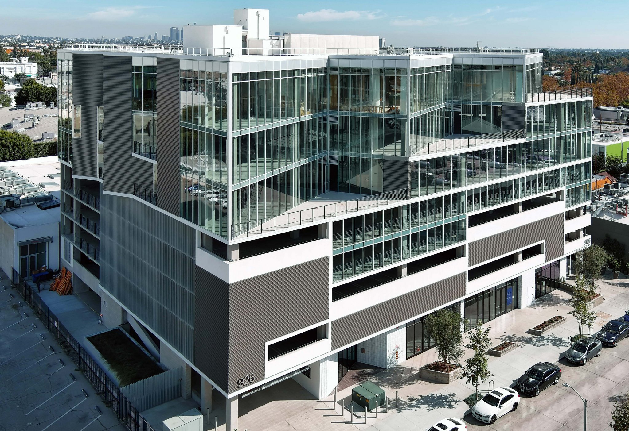 926 N. Sycamore in daytime — the glass-and-panel office building seen from above the street, its 926 numerals on the lower corner above the parking entry